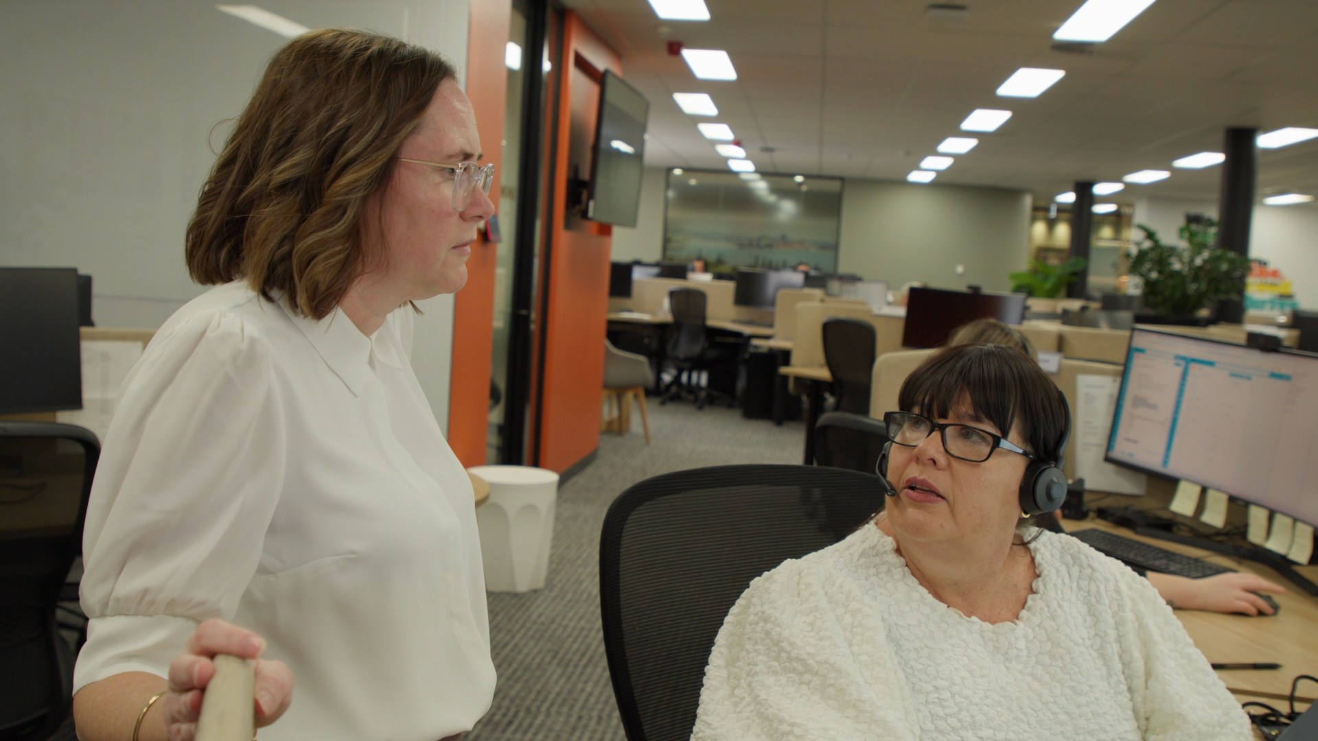Two people talking one standing one sitting at a desk trying to solve a problem